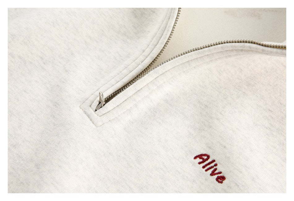 Close-up of an off-white heathered garment’s zipper and red “alive” chest embroidery.