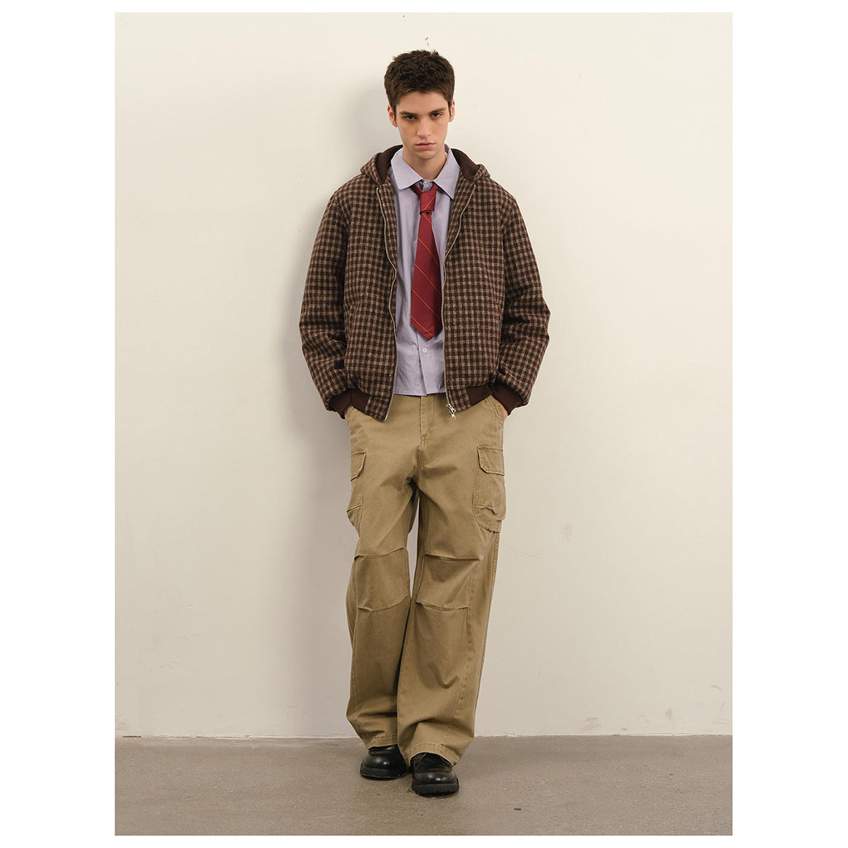 Model wearing a brown check hooded zip jacket with dark ribbed cuffs and hem, styled with tan cargo pants.