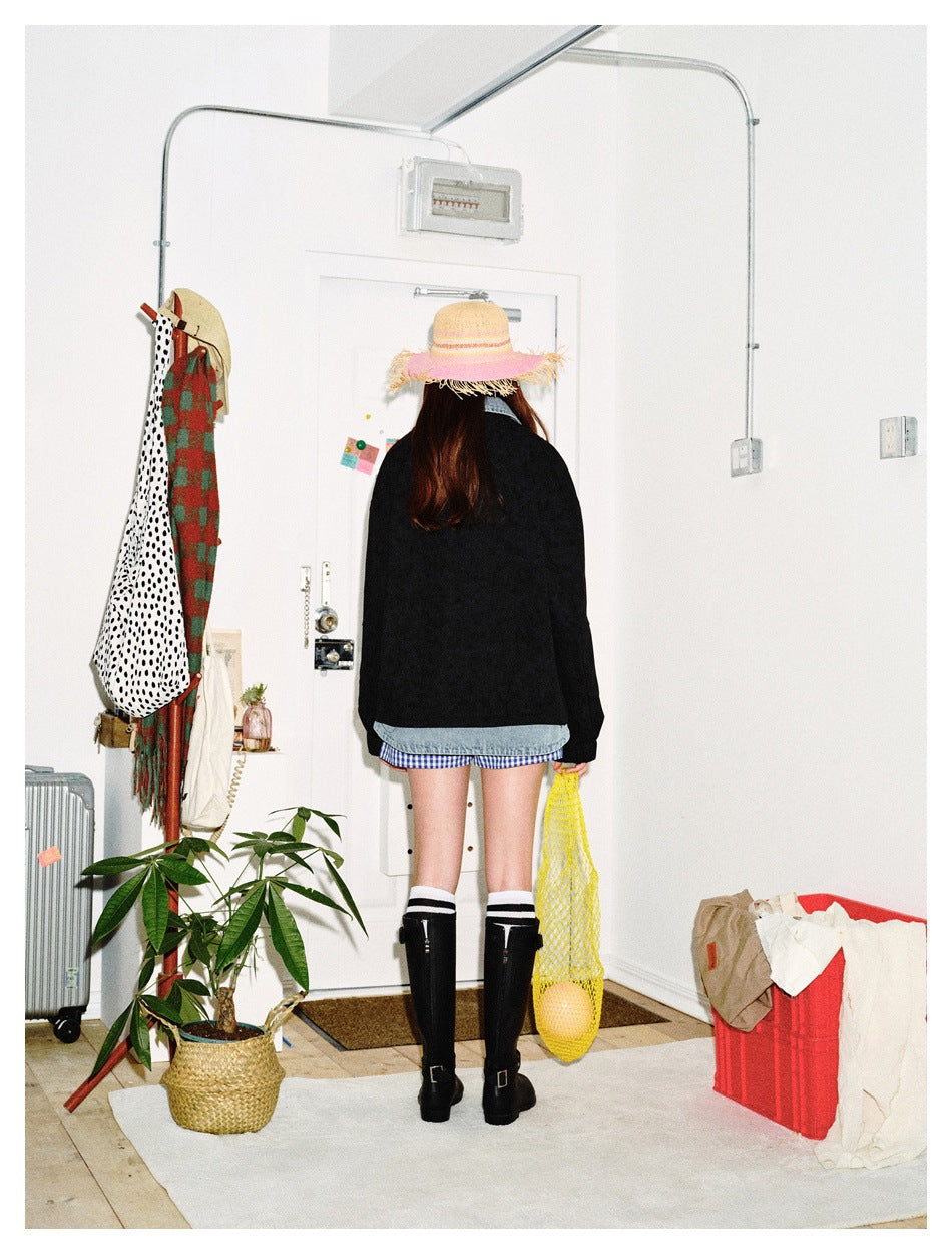 Rear view of a model wearing a black jacket with light blue denim trim, shorts, knee-high boots, and a straw hat.