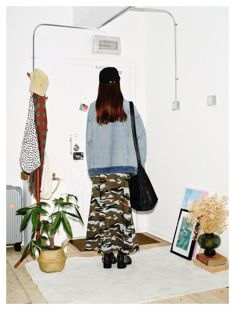 Back view of a model wearing a light-wash denim jacket and long camouflage skirt.