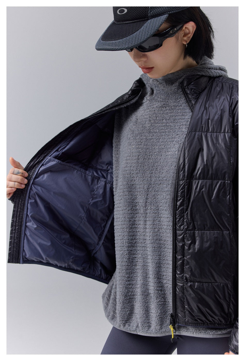 Close-up of a model wearing a black quilted jacket open over a gray fleece top, showing its dark lining.