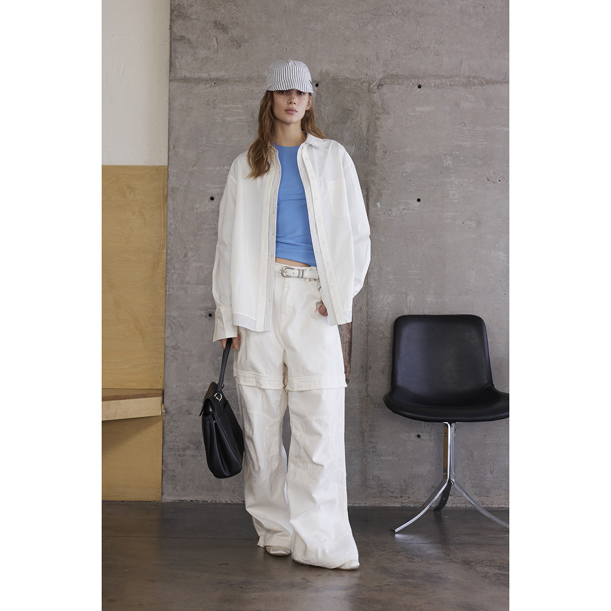 Front view of a model in a white oversized shirt and wide-leg trousers over a blue top, with a striped cap.