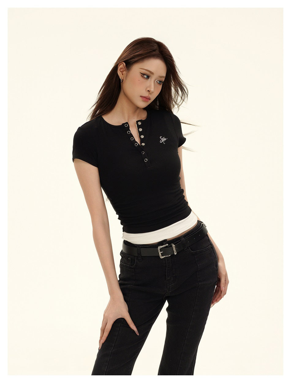 Framed angled view of a model wearing a fitted black short-sleeve top with a metal-eyelet neckline and black jeans.