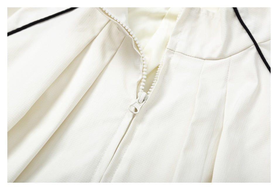 Close-up of the ivory jacket's chunky front zipper, collar, pleats, and black piping.