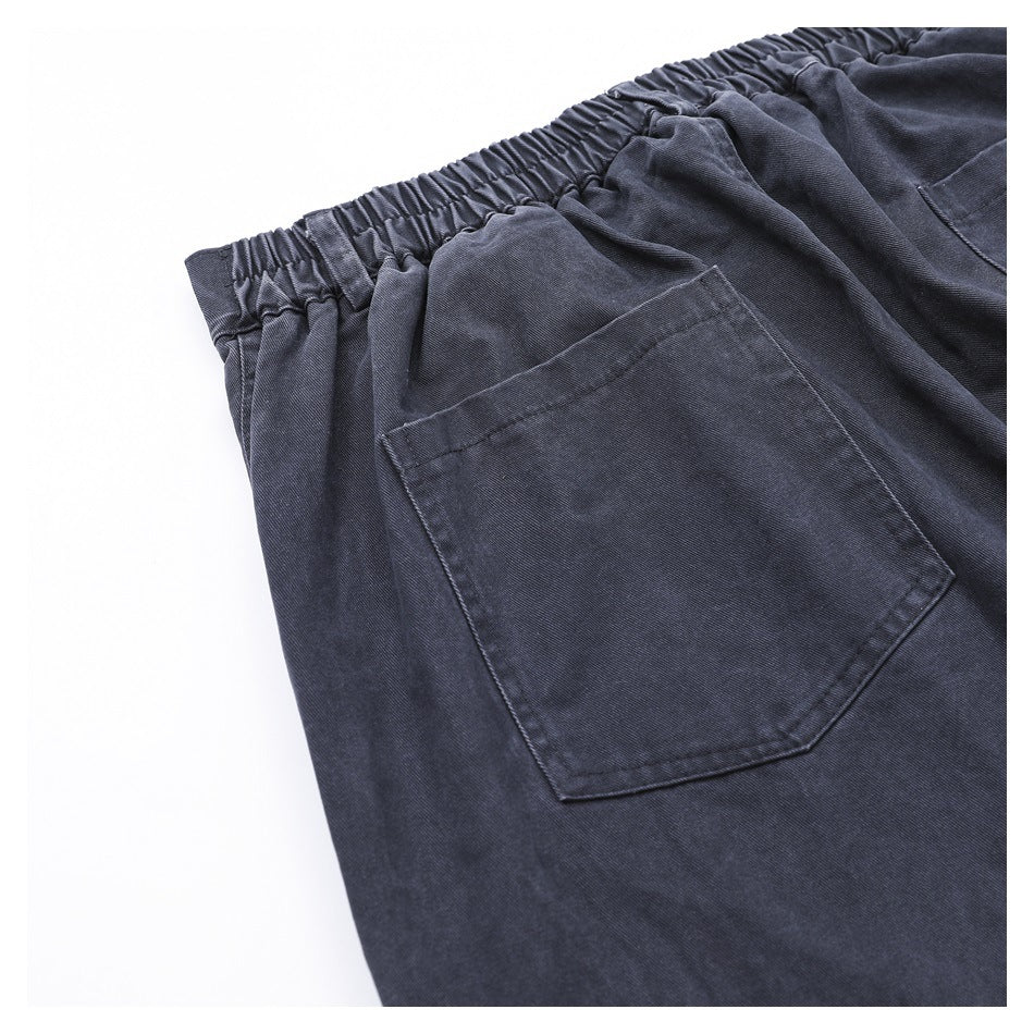 Close-up of dark charcoal pants showing the gathered elastic waistband and a stitched pocket.