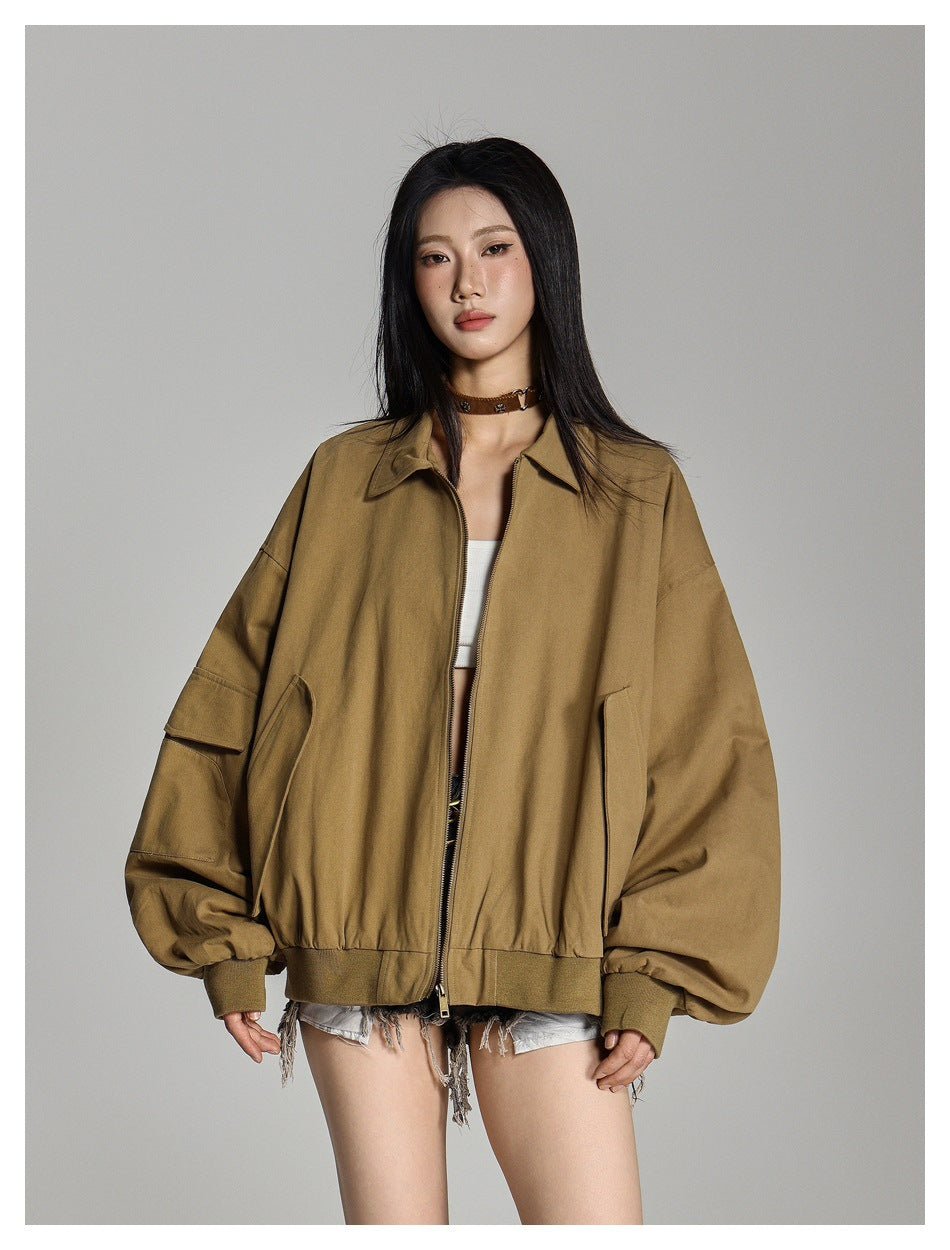 Model wearing an oversized tan-brown zip jacket with a pointed collar, roomy sleeves, and flap and welt pockets.