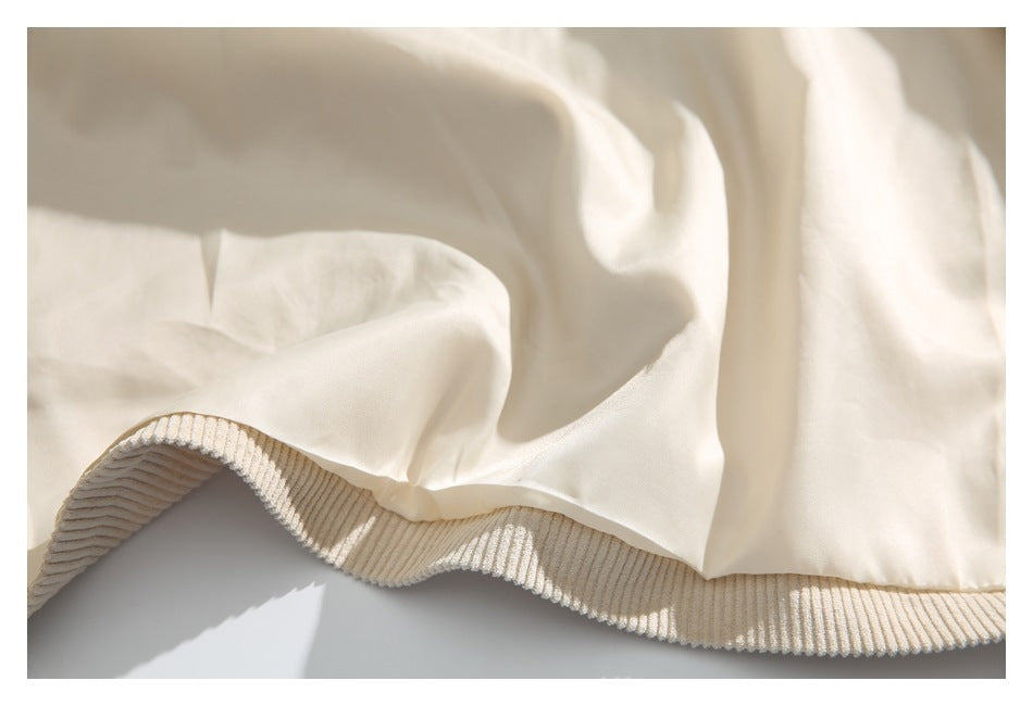 Close-up of a cream garment with a softly draped body and a wide ribbed hem.