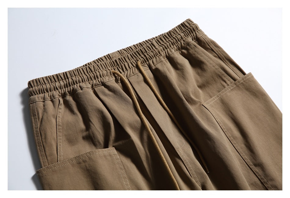 Close-up front view of brown cargo pants showing the elastic waistband, drawcords, and large patch pockets.