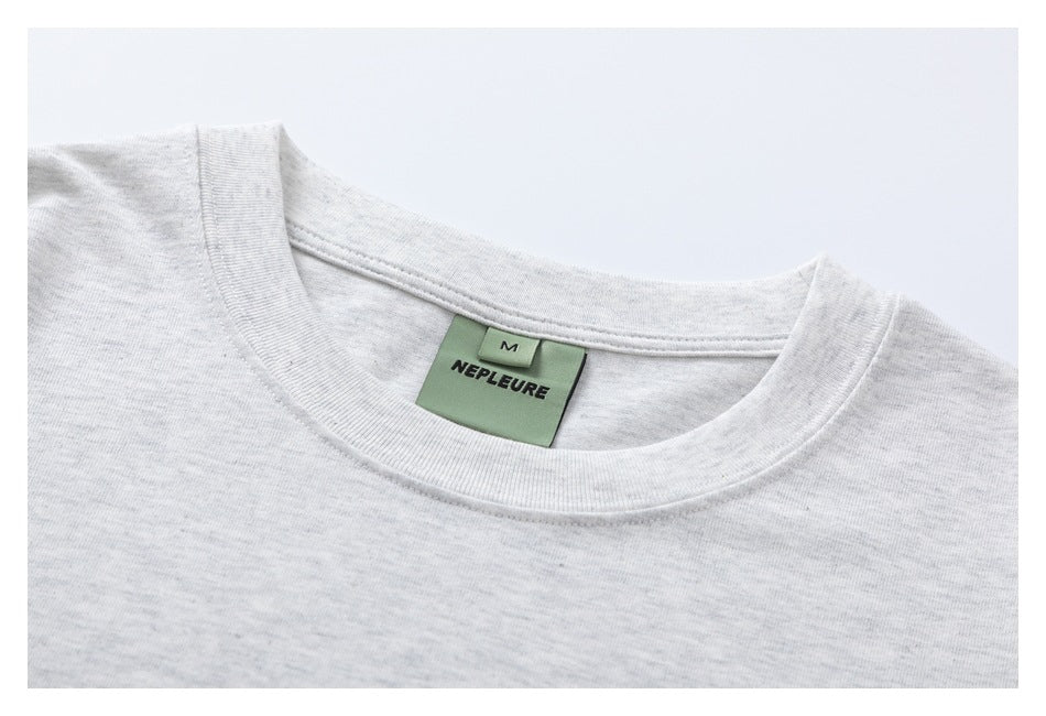 Close-up of a light heather gray T-shirt crew neck with a green NEPLEURE size M label.