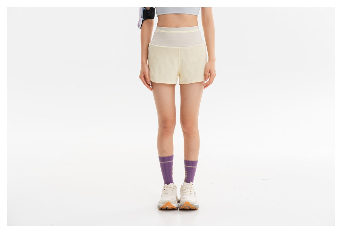 Cropped view of a model wearing cream running shorts with a high, light-colored waistband.