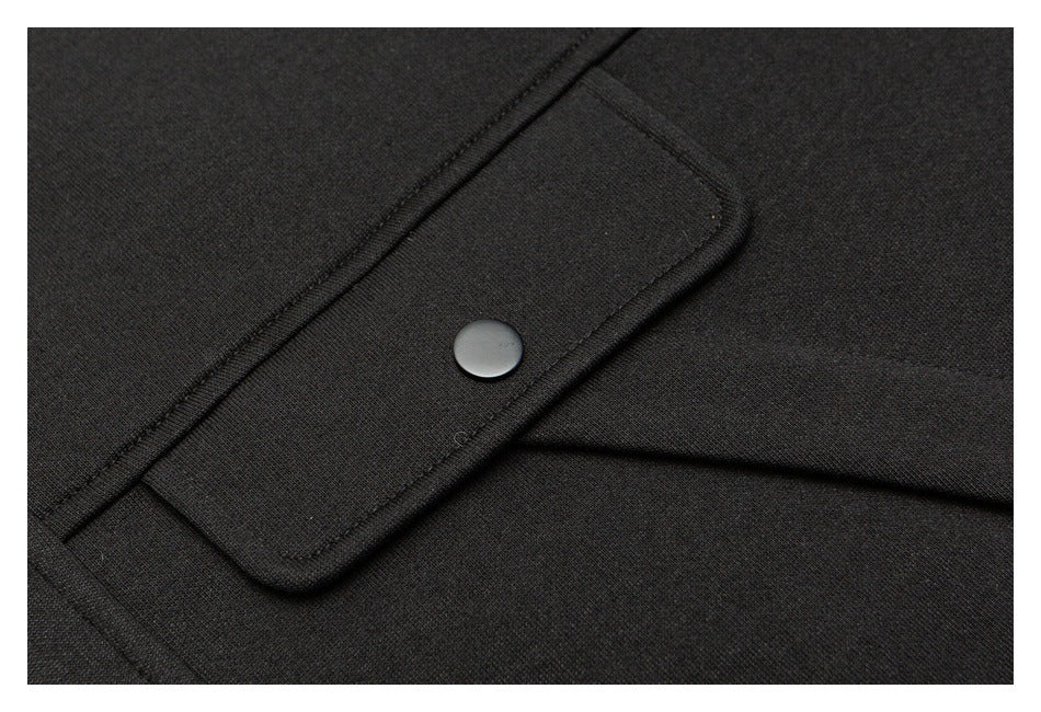 Close-up of a black garment's rectangular flap pocket with a dark snap closure.