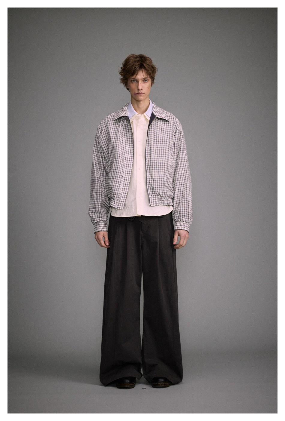 Model wearing the cropped check reversible jacket open over a cream shirt with wide dark trousers, front view