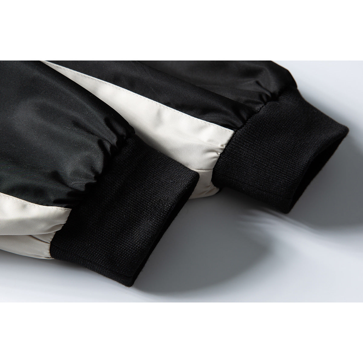 Close-up of a black ribbed cuff beside a light contrasting panel on a jacket sleeve.