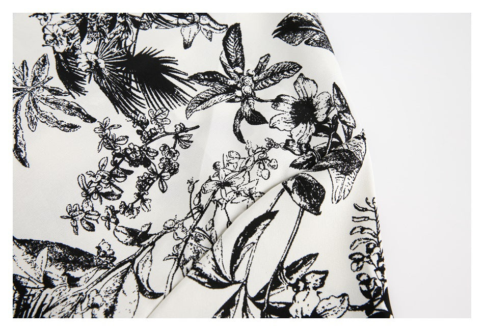 Close-up of ivory fabric draped to show its black botanical print of leaves and flowers.