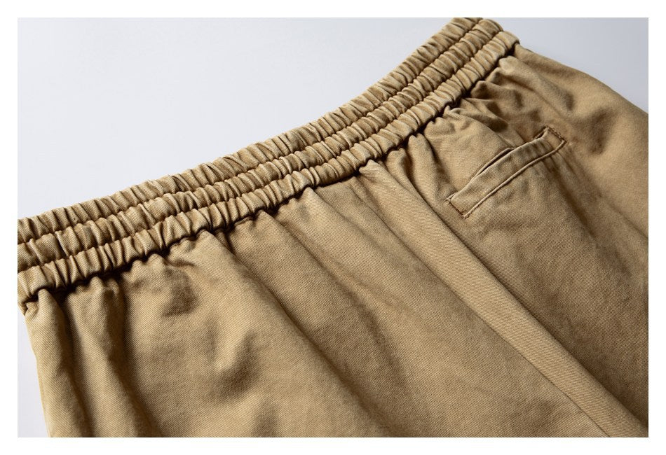 Close-up of tan trousers showing the gathered elastic waistband and a slanted pocket.