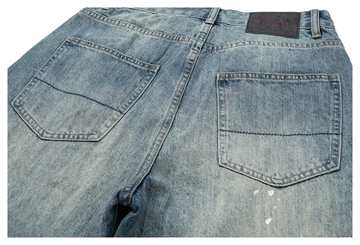 Close-up of the back of faded blue jeans, showing two stitched pockets, a waistband patch, and small white marks.