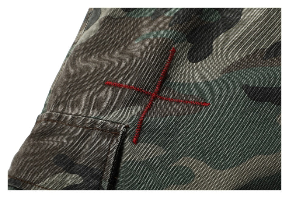 Close-up of red cross-shaped stitching beside a pocket on camouflage trousers.