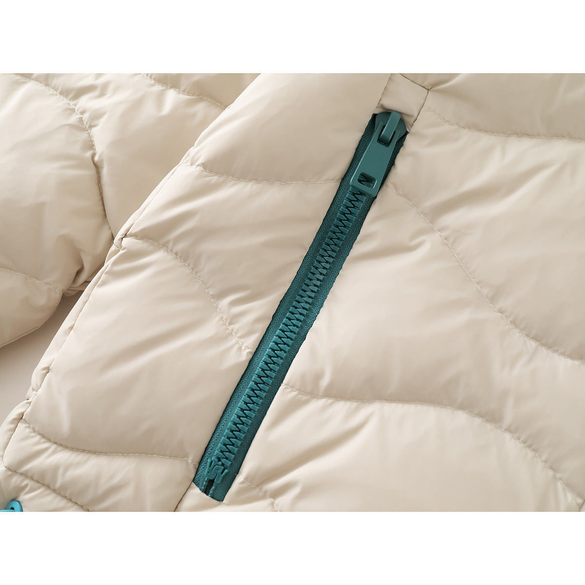 Close-up of the teal zipper and quilted ivory fabric on a jacket.