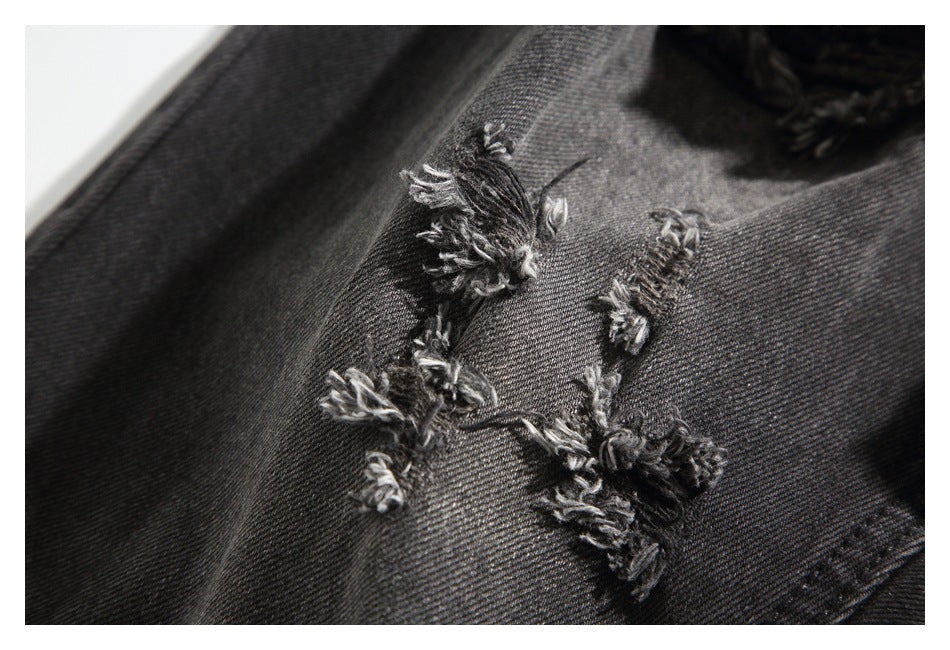 Close-up of frayed black denim distressing with loose threads.