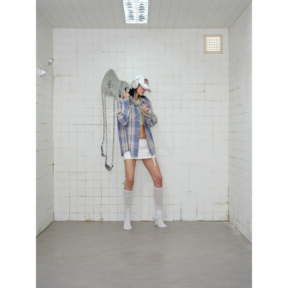 Model wearing an open blue plaid shirt with a pale yellow crop top, white mini skirt, and knee-high socks.