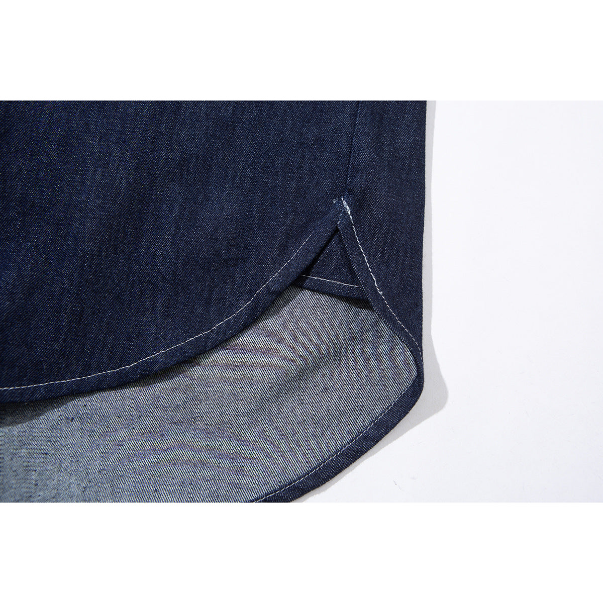 Close-up of the curved hem of a dark indigo shirt, showing contrast stitching and the lighter reverse side.