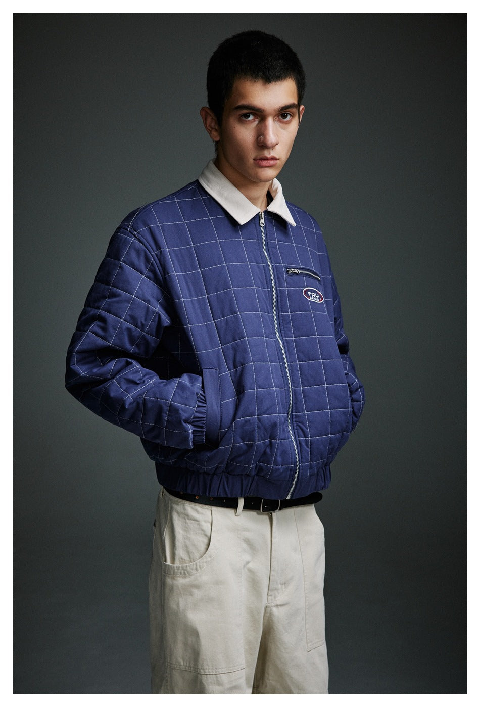 Front view of a model wearing a navy grid-quilted jacket with a cream collar and zip closure.