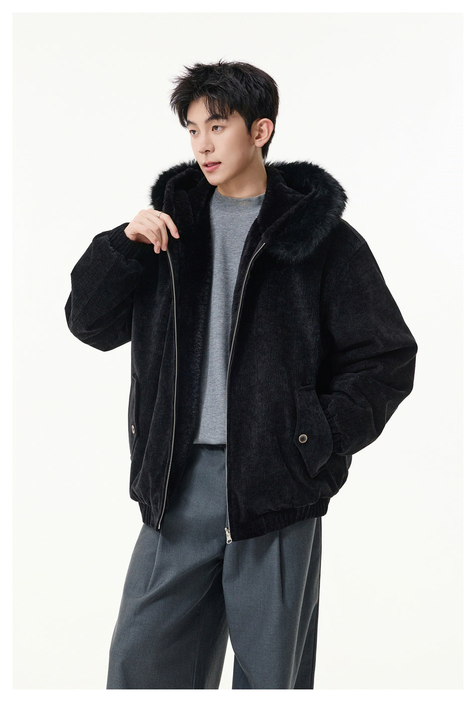 Front view of a model wearing a black hooded jacket with plush hood trim, zipper, and buttoned flap pockets.