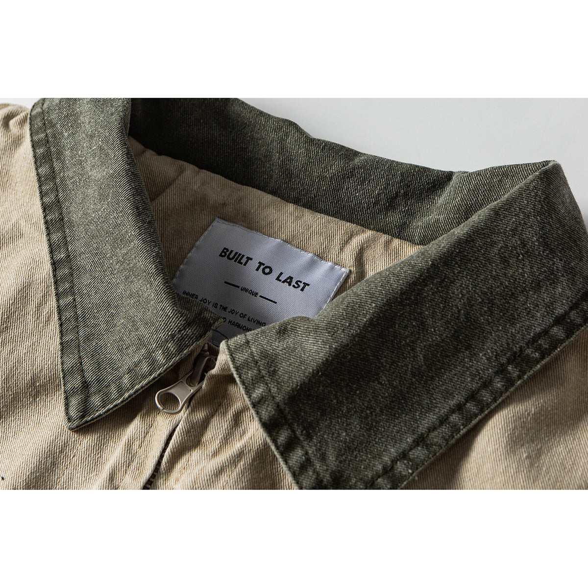 Close-up of a beige jacket with a dark washed collar, front zipper, and an inner label reading “BUILT TO LAST.”