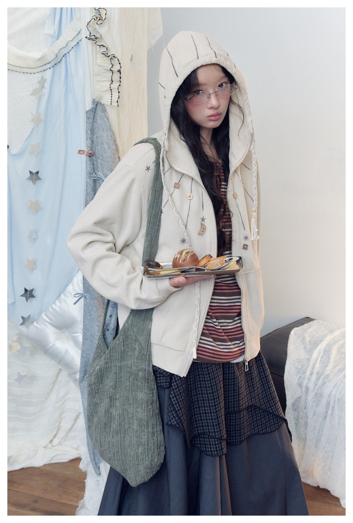 Closer view of a model wearing an ivory zip-up hooded jacket with gray star and moon motifs and braided trim.