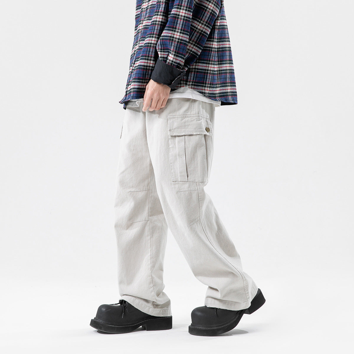Side view of a model wearing loose light gray cargo pants with a flap thigh pocket and black shoes.