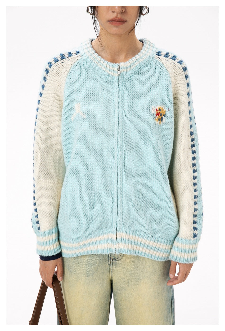 Close view of the pale blue cardigan's zip front, cream raglan sleeves, navy sleeve edging, and chest motifs.
