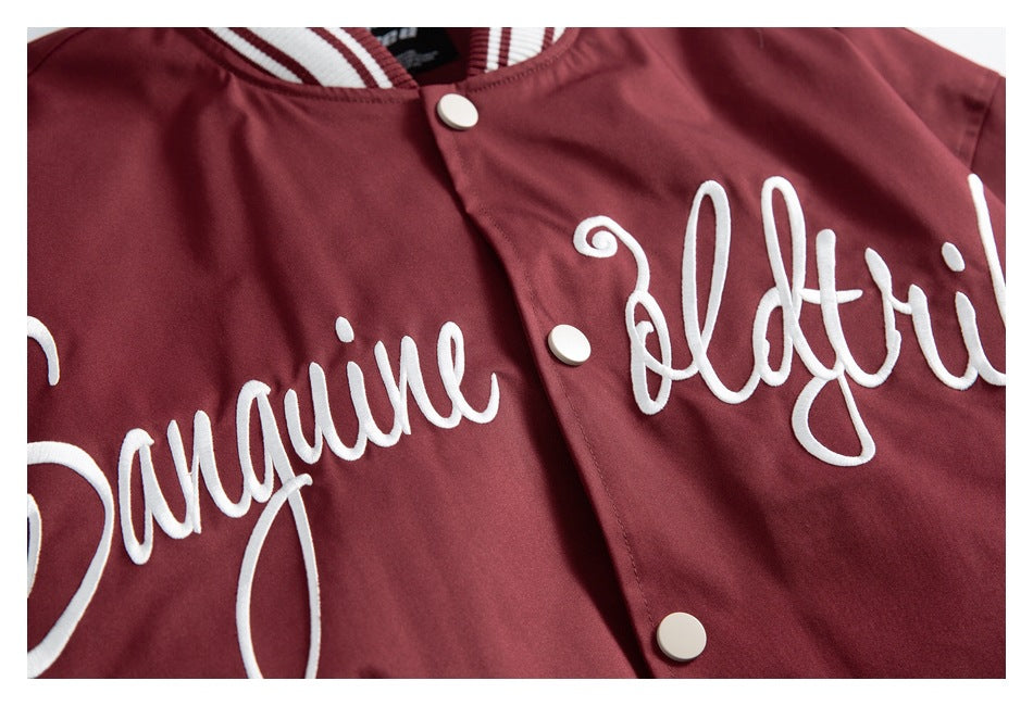 Close-up of white cursive embroidery and white snaps on the burgundy jacket front.