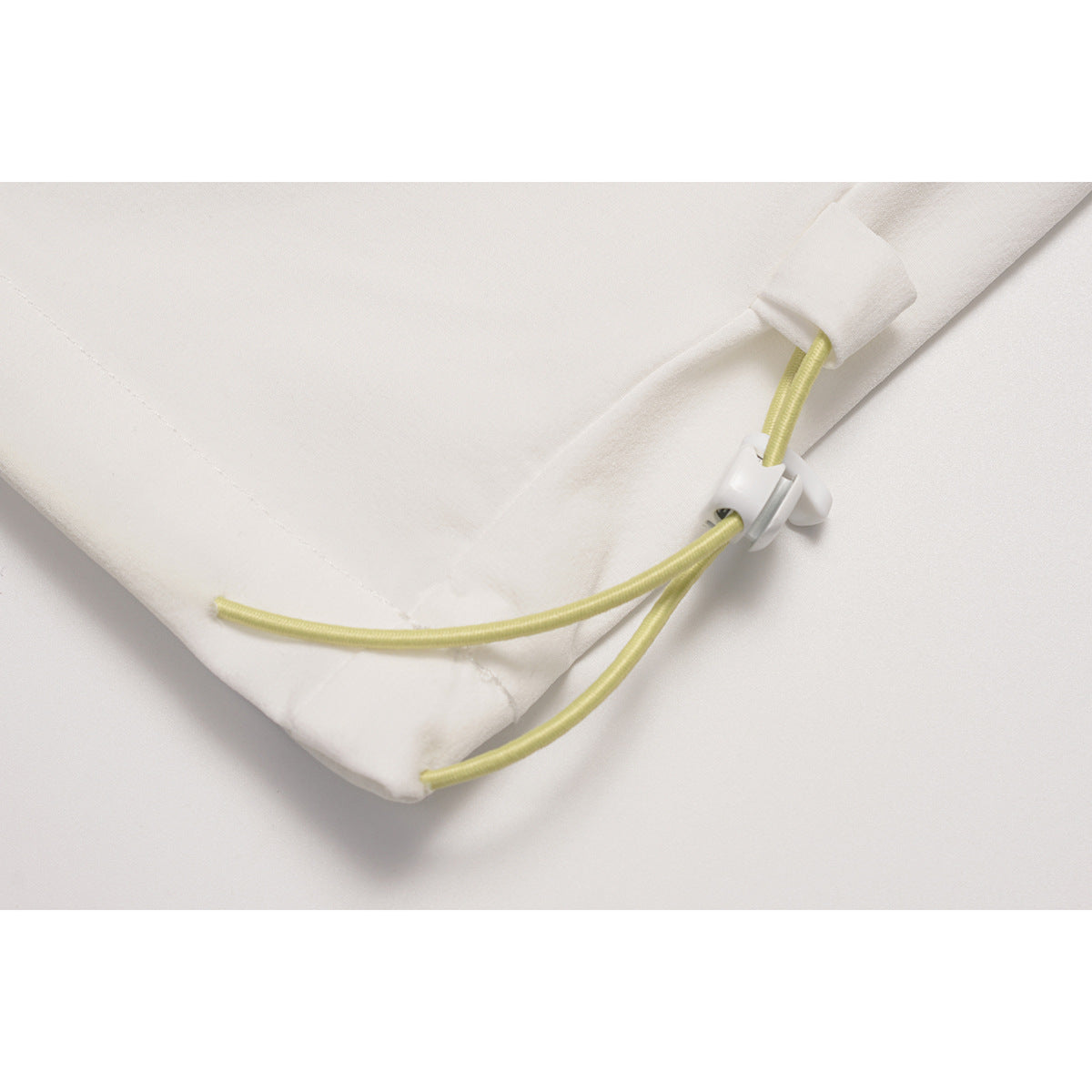 Close-up of a white pant-leg hem with a yellow cord and plastic toggle.