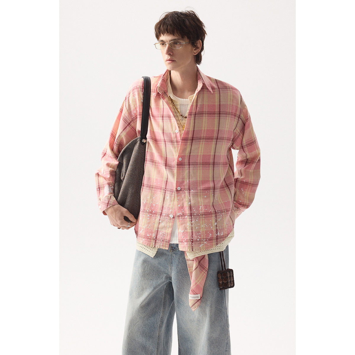 Model wearing a pink plaid button-up shirt with white splatter details, layered over a cream knit top.