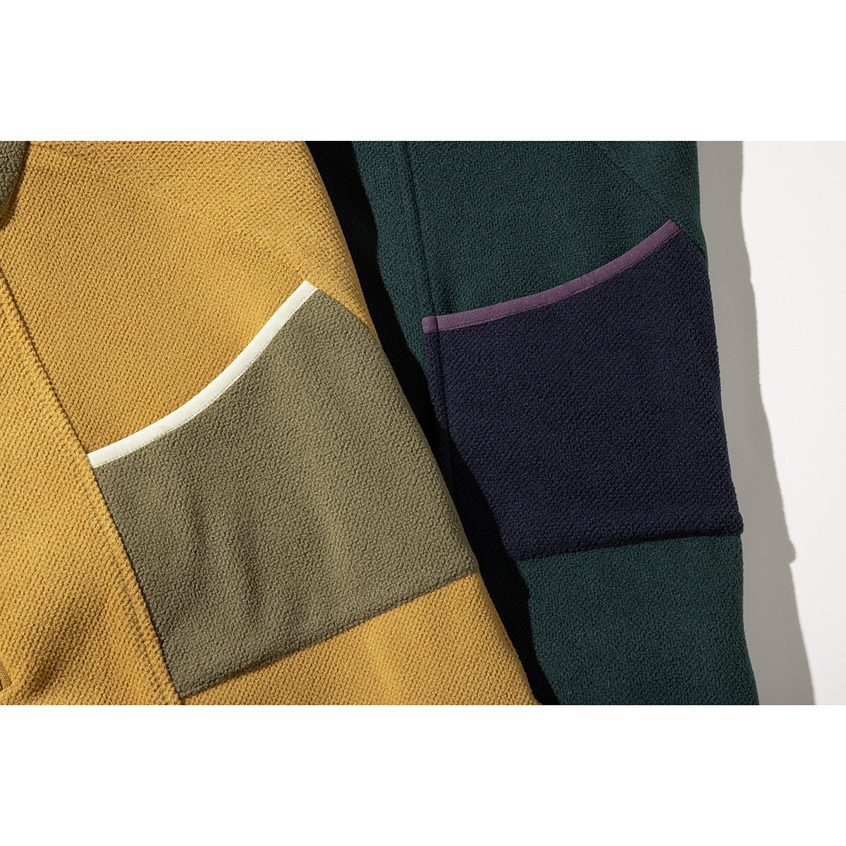 Close-up of color-block chest pockets on mustard and dark teal hooded jackets.