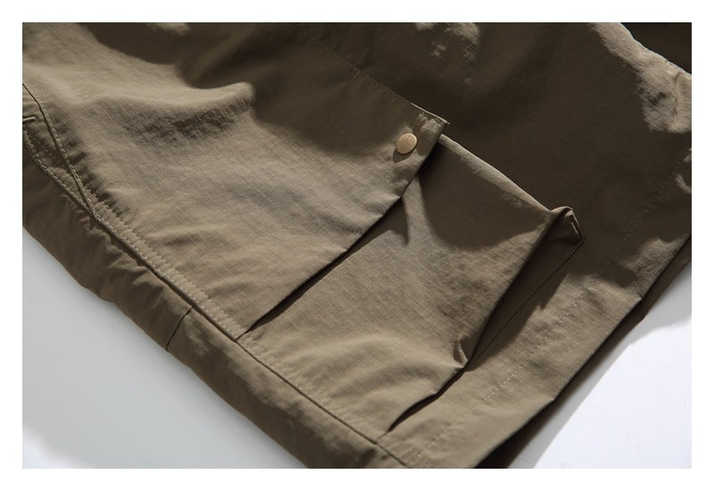 Close-up of a tan snap on an overlapping flap pocket of an olive-brown garment.