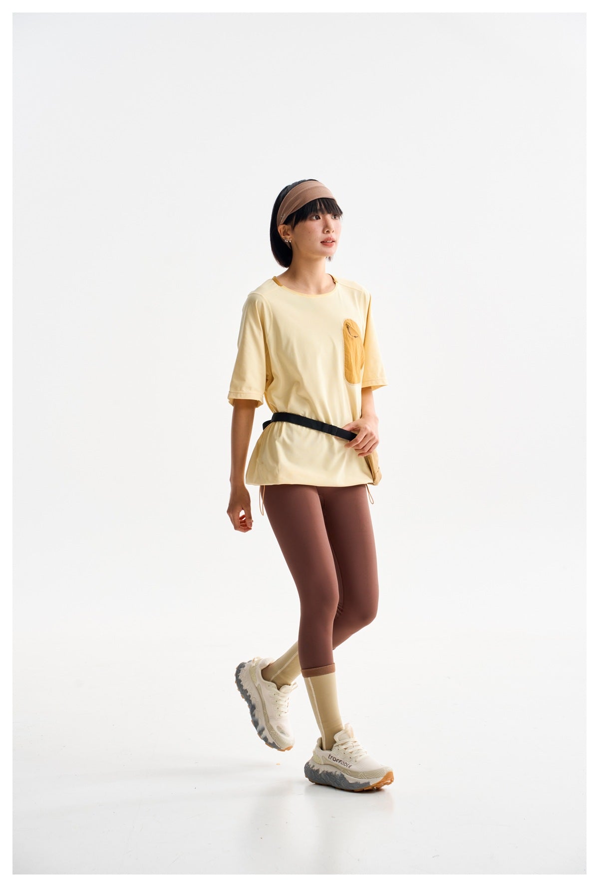 Model in a pale yellow short-sleeve top with a mustard chest pocket and brown leggings, shown in a walking pose.