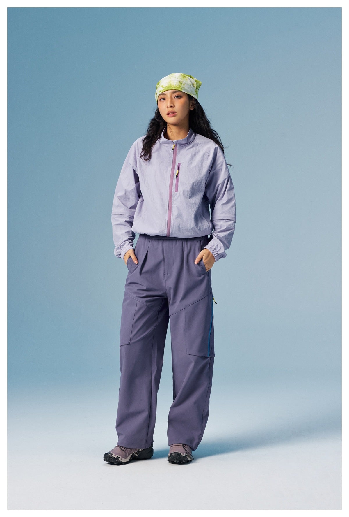 Full-length model wearing a pale lavender zip jacket with a chest pocket and slate-purple cargo pants.