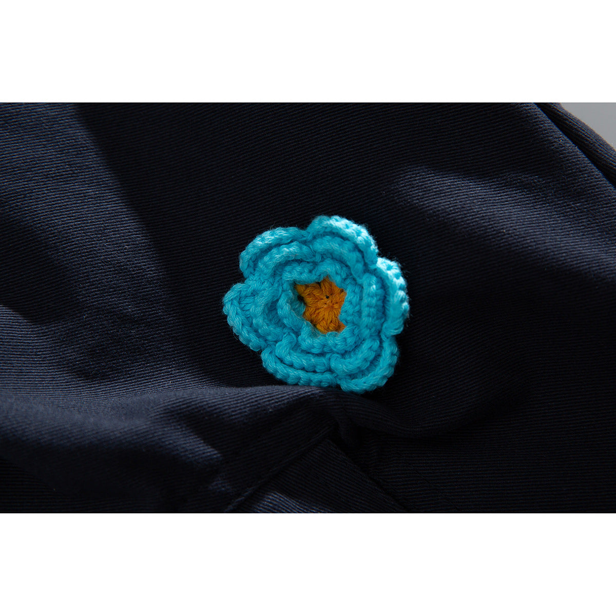Turquoise crocheted flower with a yellow center sewn onto dark navy fabric.