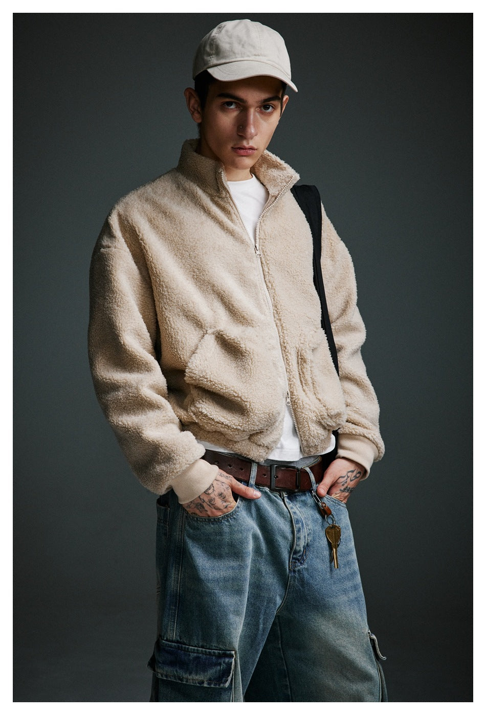 Model wearing a beige zip-up fleece jacket with a stand collar and large front pockets, shown with loose blue cargo jeans.