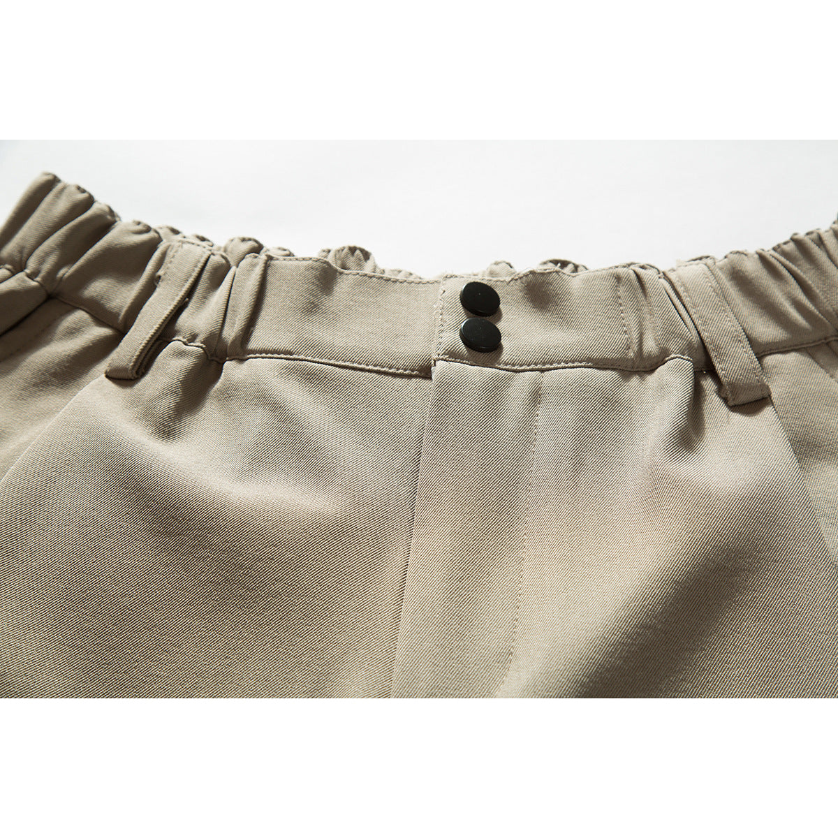 Close-up of beige shorts showing an elasticated waistband, belt loops, and two black buttons.
