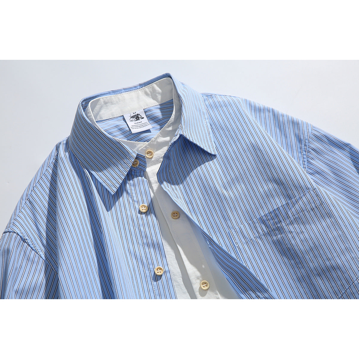 Close-up of a light blue striped button-up shirt with a pointed collar, white inner placket, and tan buttons.