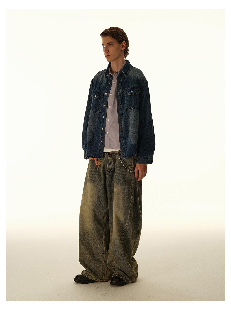 Model wearing an oversized dark indigo denim shirt with chest pockets and wide, faded olive-gray jeans, shown at an angle.
