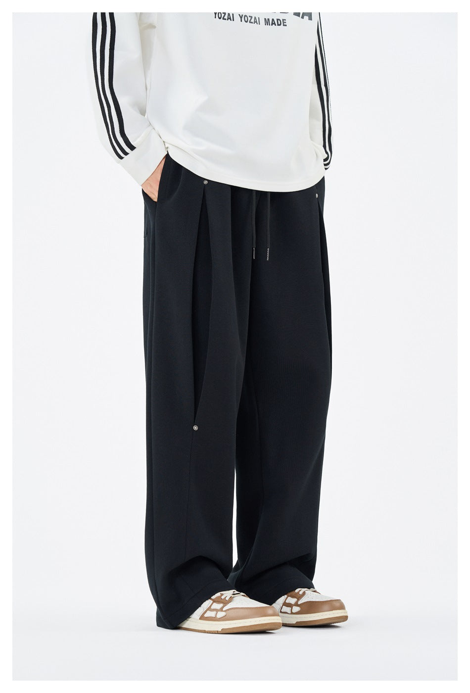Front view of a model wearing loose black wide-leg trousers with a drawstring waist and snap-button panel.