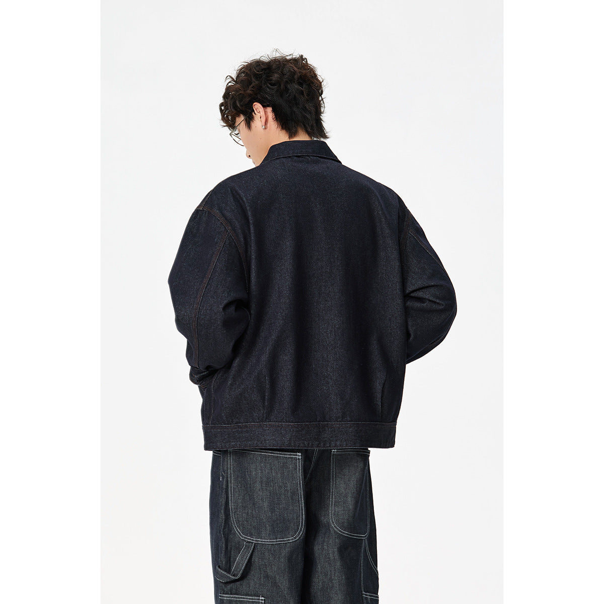 Back view of a model wearing a dark indigo denim jacket with a wide hem and relaxed sleeves.
