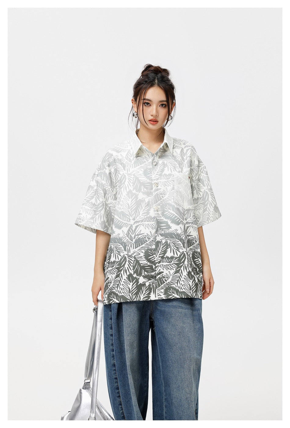 Model wearing a loose white button-up shirt with gray tropical leaf print, paired with blue jeans.