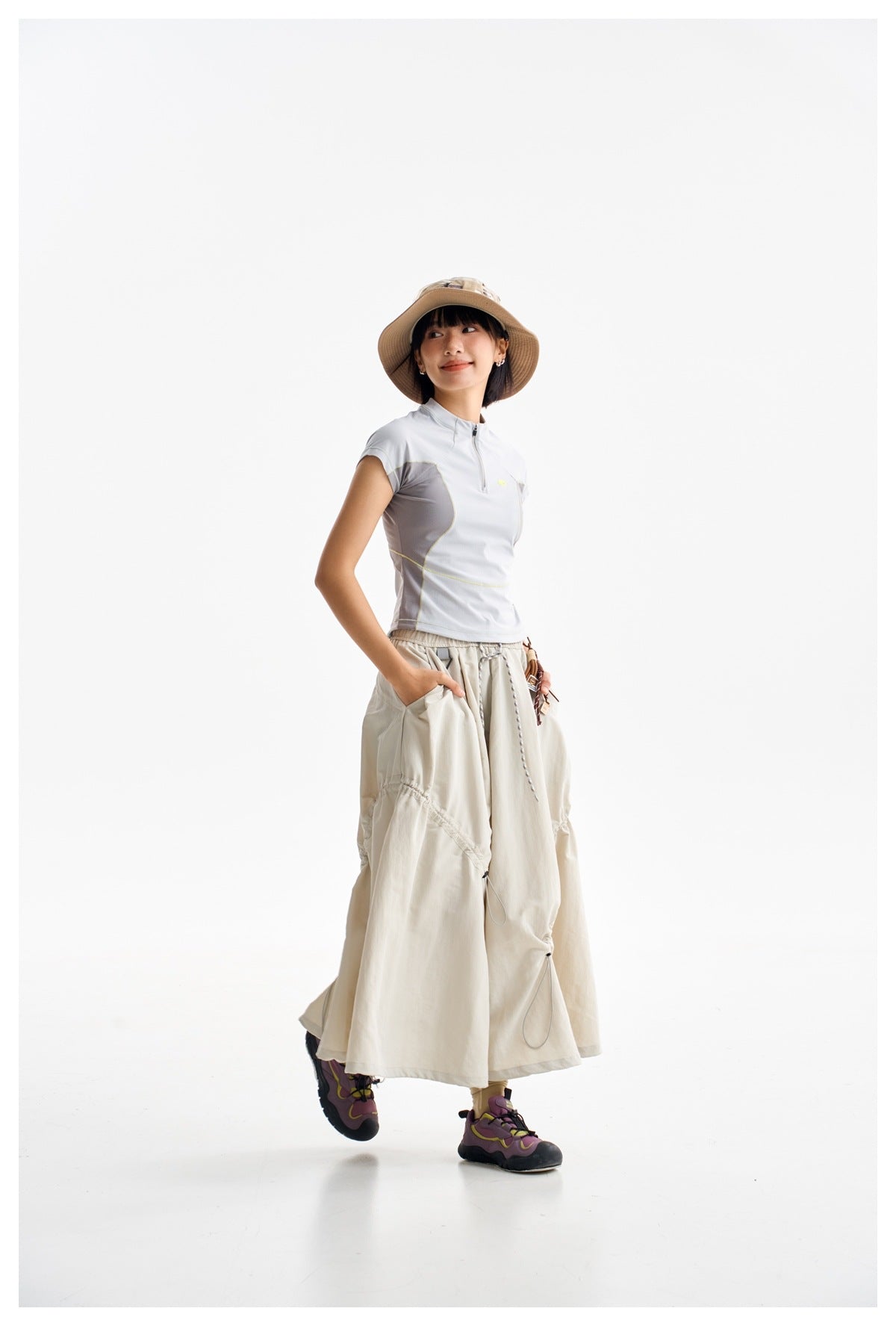 Model wearing a pale gray quarter-zip top with darker side panels and a long cream skirt.