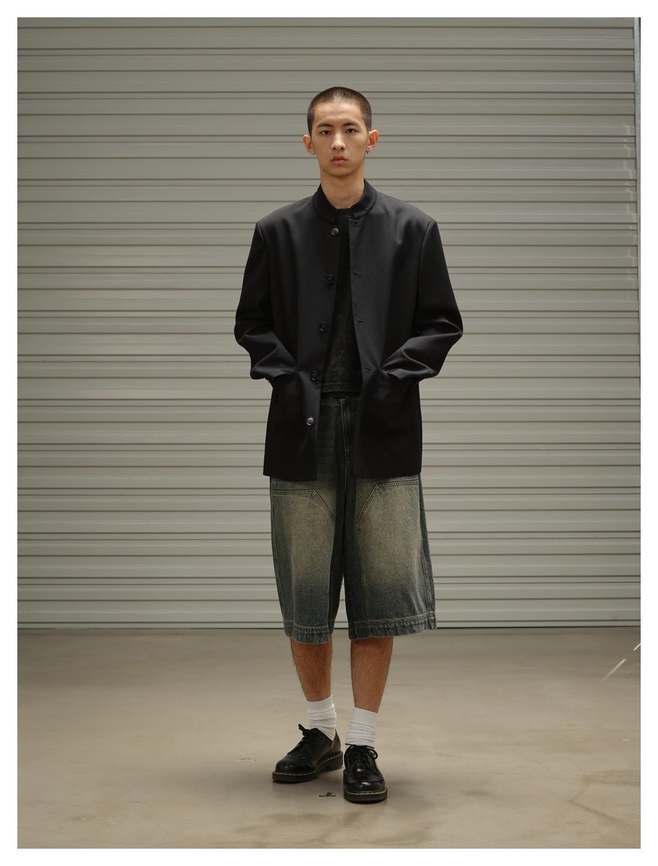 Front view of a model wearing a buttoned black stand-collar jacket with faded denim shorts.