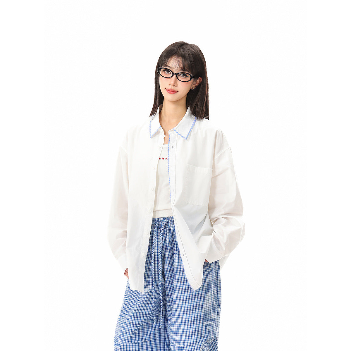 Model wearing an open white shirt with blue-trimmed collar over a white top and loose blue checked trousers.