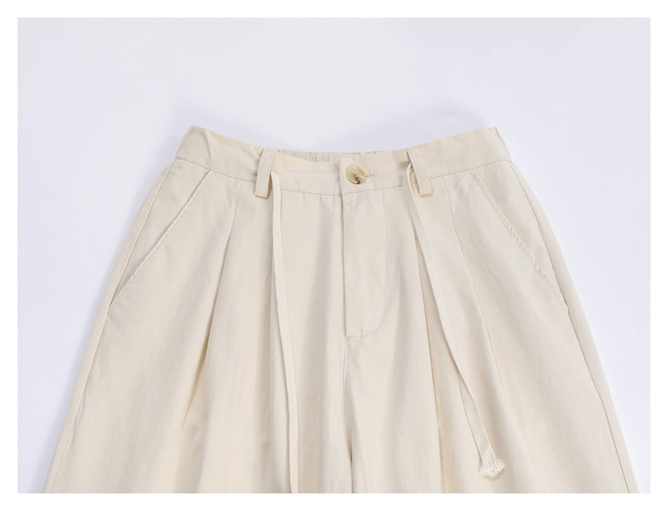 Upper front of ivory wide-leg trousers with a button closure, belt loops, pleats, slanted pockets and a drawstring.